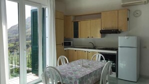 A kitchen with wooden cabinets, a microwave, a refrigerator, and a dining table with chairs. - Olive Tree "Villa Nunzia" (Barano D'ischia)