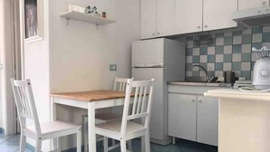Una cucina piccola e pulita con mobili bianchi, un tavolo di legno e due sedie bianche.
