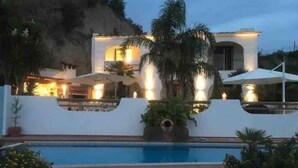 Una villa moderna con piscina, circondata da palme e con vista sulle montagne.