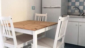 Una cocina pequeña con un refrigerador blanco, una mesa de madera y sillas blancas.