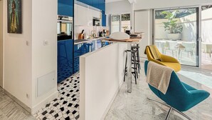 A modern kitchen with blue cabinets, a central island, and a dining area with a yellow chair.