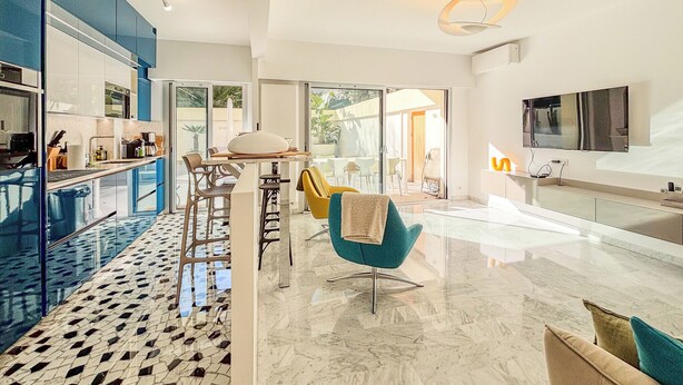 A modern kitchen with a dining area, large windows, and a TV mounted on the wall.