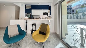A modern kitchen with blue cabinets, a white countertop, and a yellow chair. There is a window with a view of buildings and cacti outside.