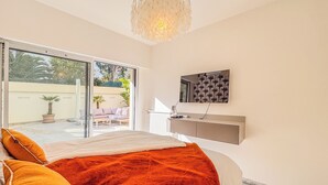 A bedroom with a large bed, a sliding glass door leading to an outdoor area, a mounted TV, and a marble floor.