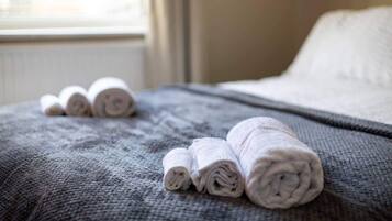 Een opgemaakt bed met opgerolde witte handdoeken en een grijze deken.