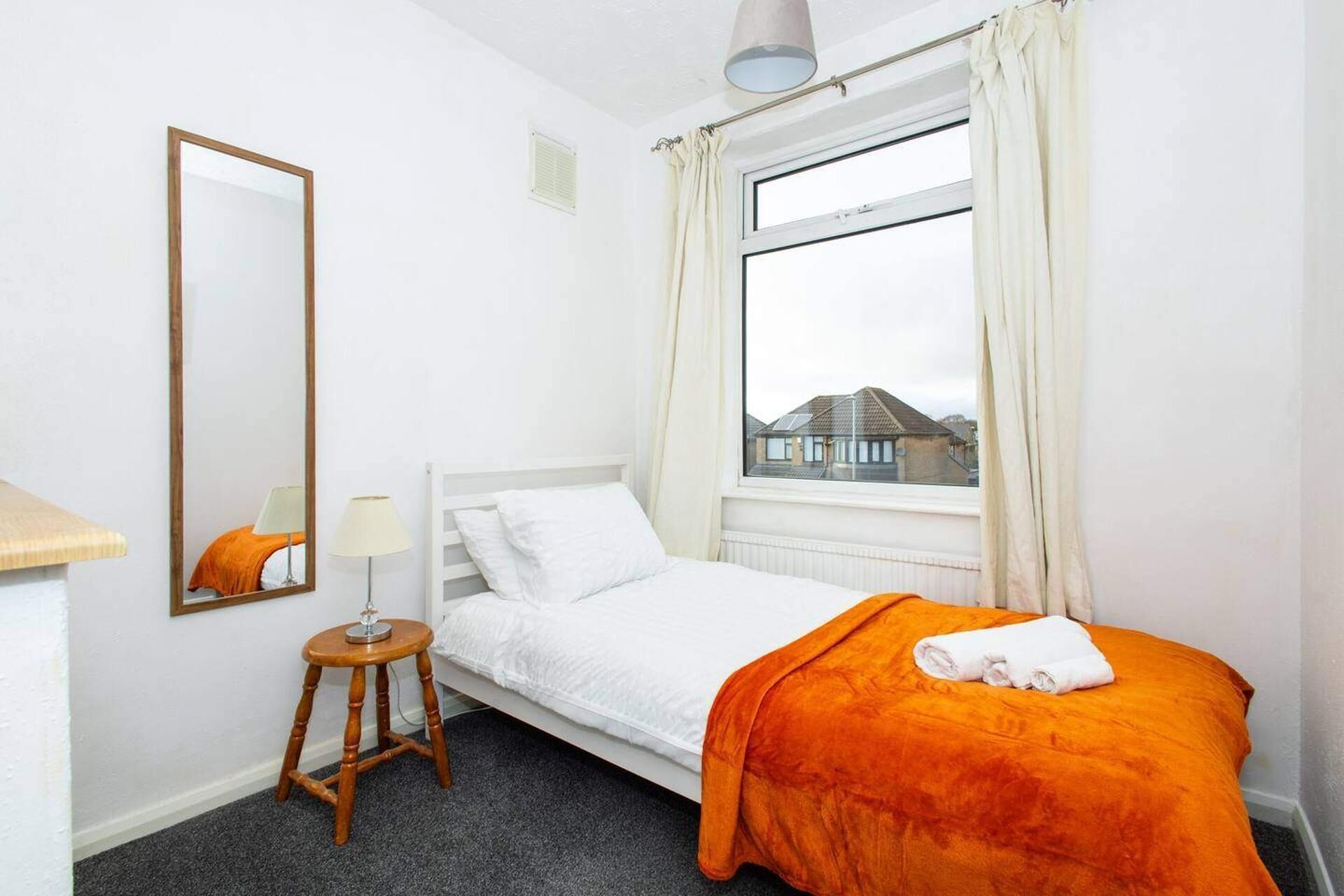 A small, clean room with a bed, a bedside table, a lamp, and a window with curtains.