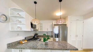 Une cuisine moderne dotée d’un plan de travail en granit, de meubles blancs, d’un réfrigérateur en acier inoxydable et de deux luminaires suspendus.
