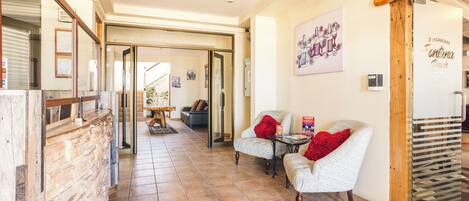 Un hall de hotel con una pared de piedra, dos sillones tapizados con cojines rojos, un letrero de madera sobre la entrada y un piso de baldosas.