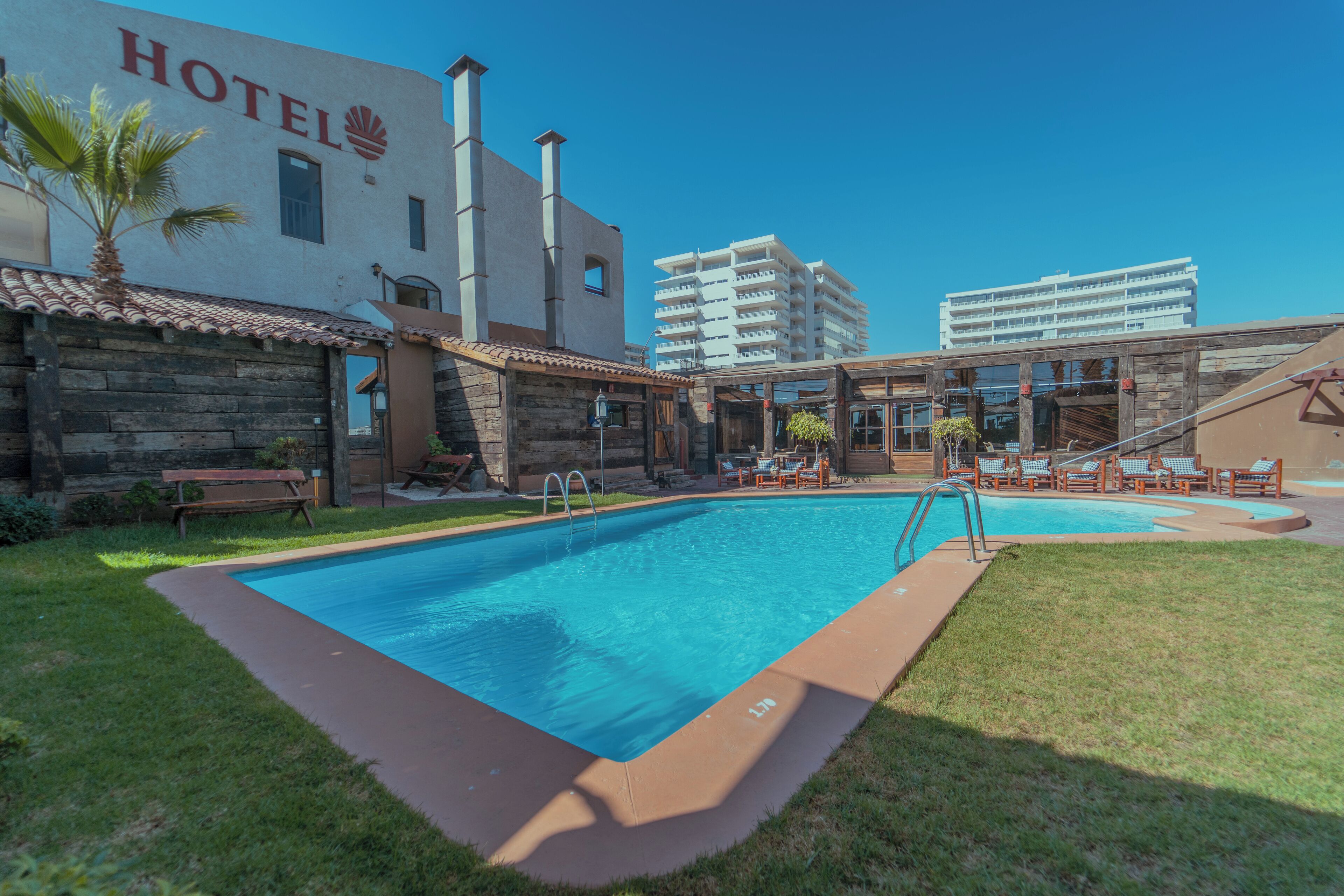 A hotel with a swimming pool, outdoor seating, and a view of a tall building in the background.