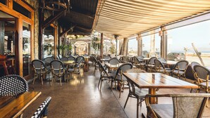 An outdoor dining area with wooden tables and wicker chairs, a striped awning, and a view of the beach. - Hotel Canto del Mar (La Serena)