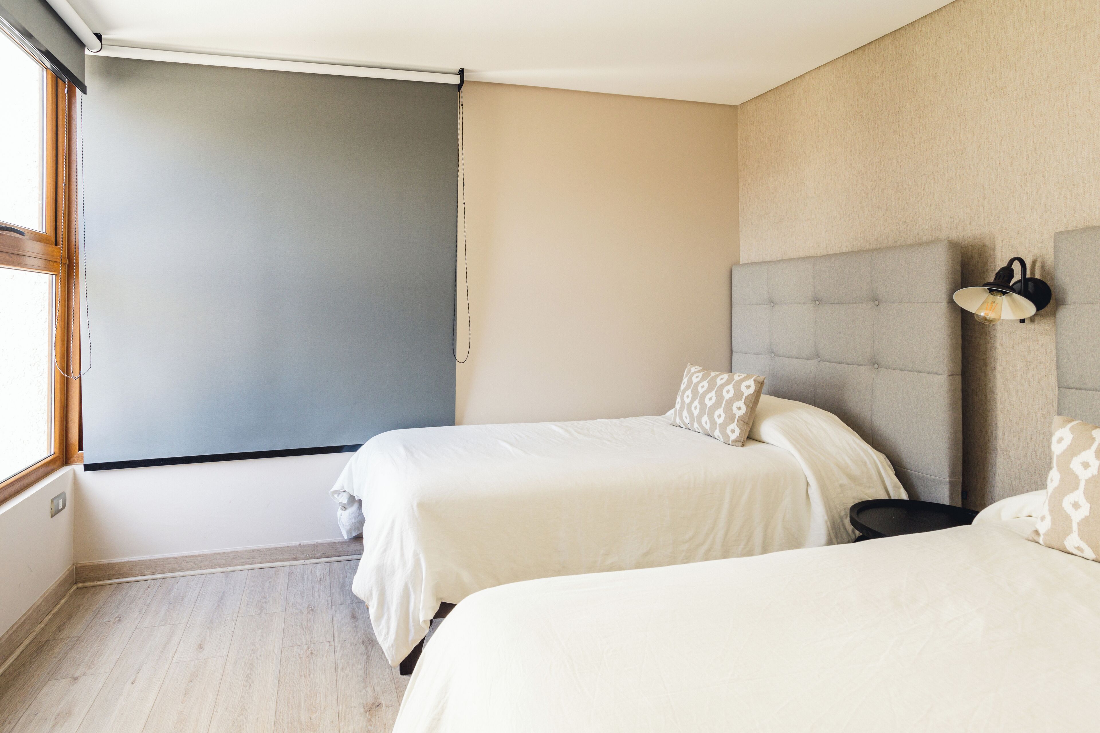 A hotel room with two beds, a large window, and a wall-mounted light fixture.