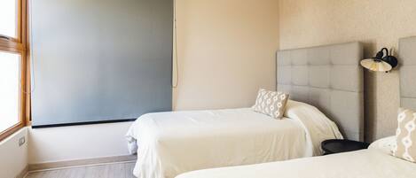 A hotel room with two beds, a large window, and a wall-mounted light fixture.