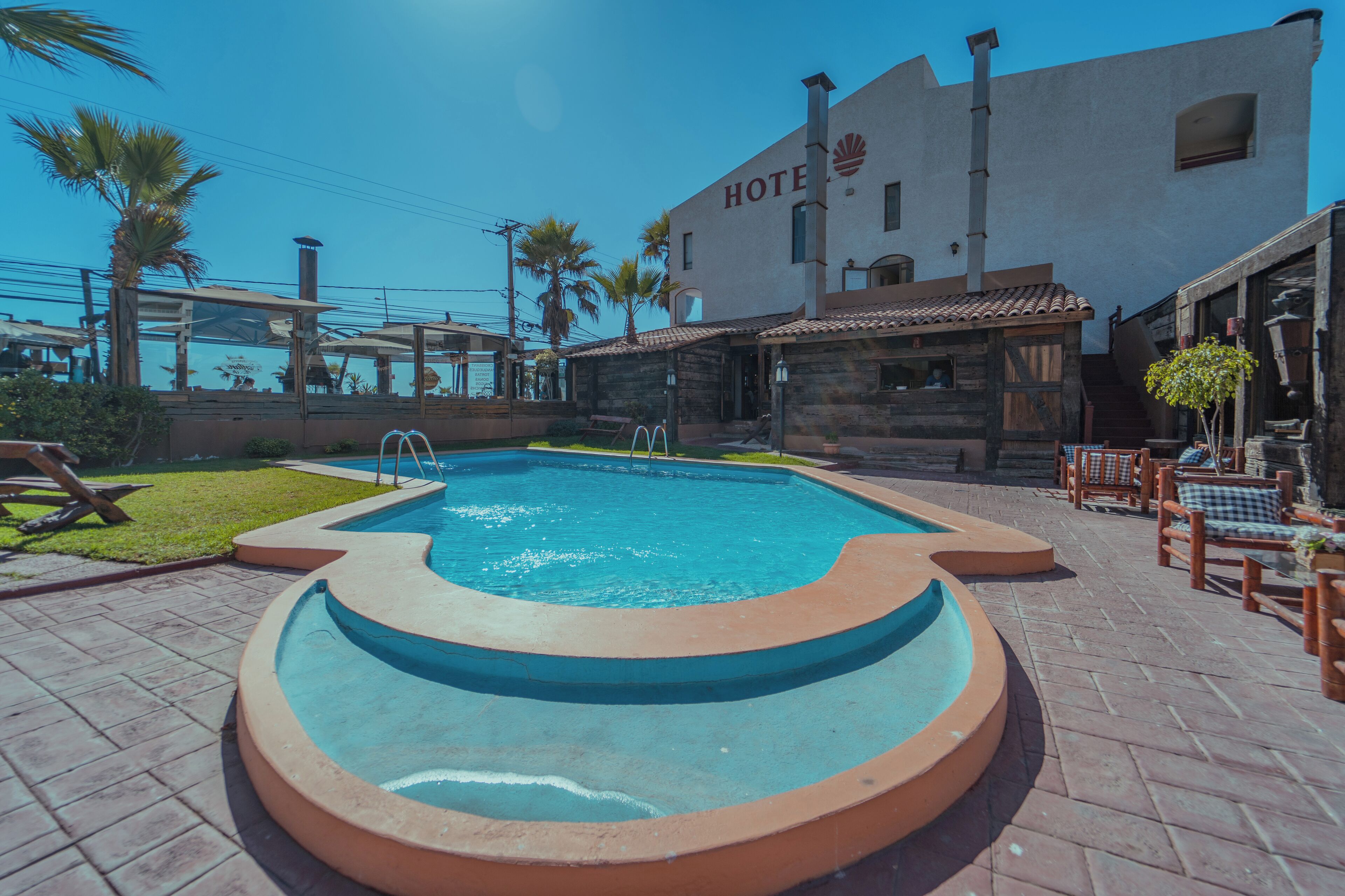 A hotel with a swimming pool, outdoor seating, and palm trees.