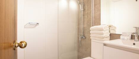 Un baño moderno con ducha envuelta en vidrio, inodoro blanco y lavamanos con espejo.