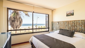 A hotel room with a large window offering a view of the beach and ocean. - Hotel Canto del Mar (La Serena)