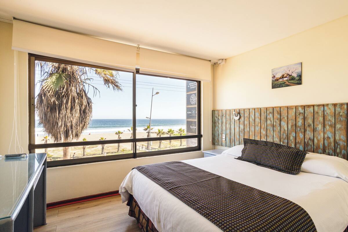 Ein Hotelzimmer mit großem Fenster und Blick auf Strand und Meer.