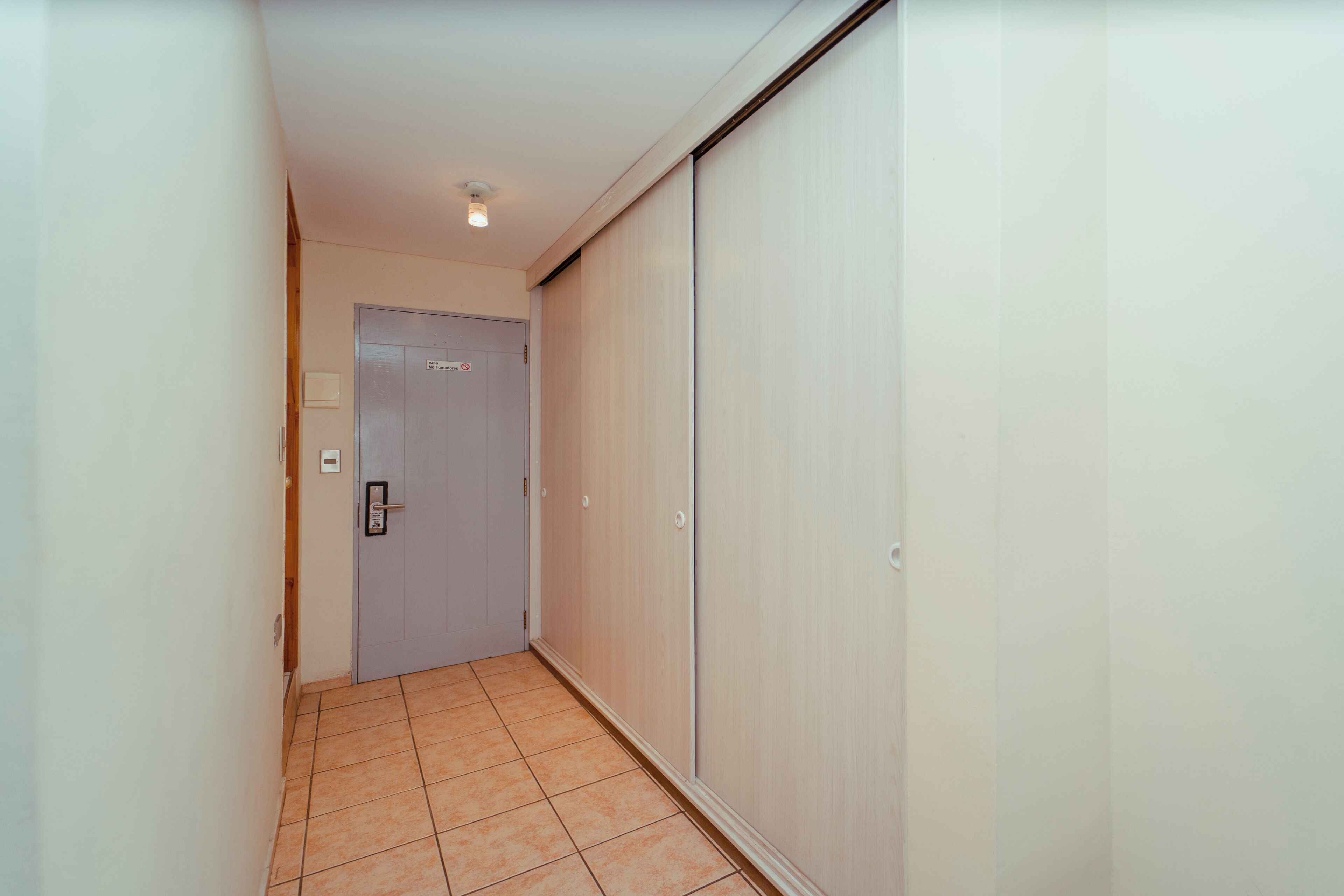 A narrow hallway with a door at the end, a light fixture on the ceiling, and a tiled floor.