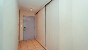 A narrow hallway with a door at the end, a light fixture on the ceiling, and a tiled floor.