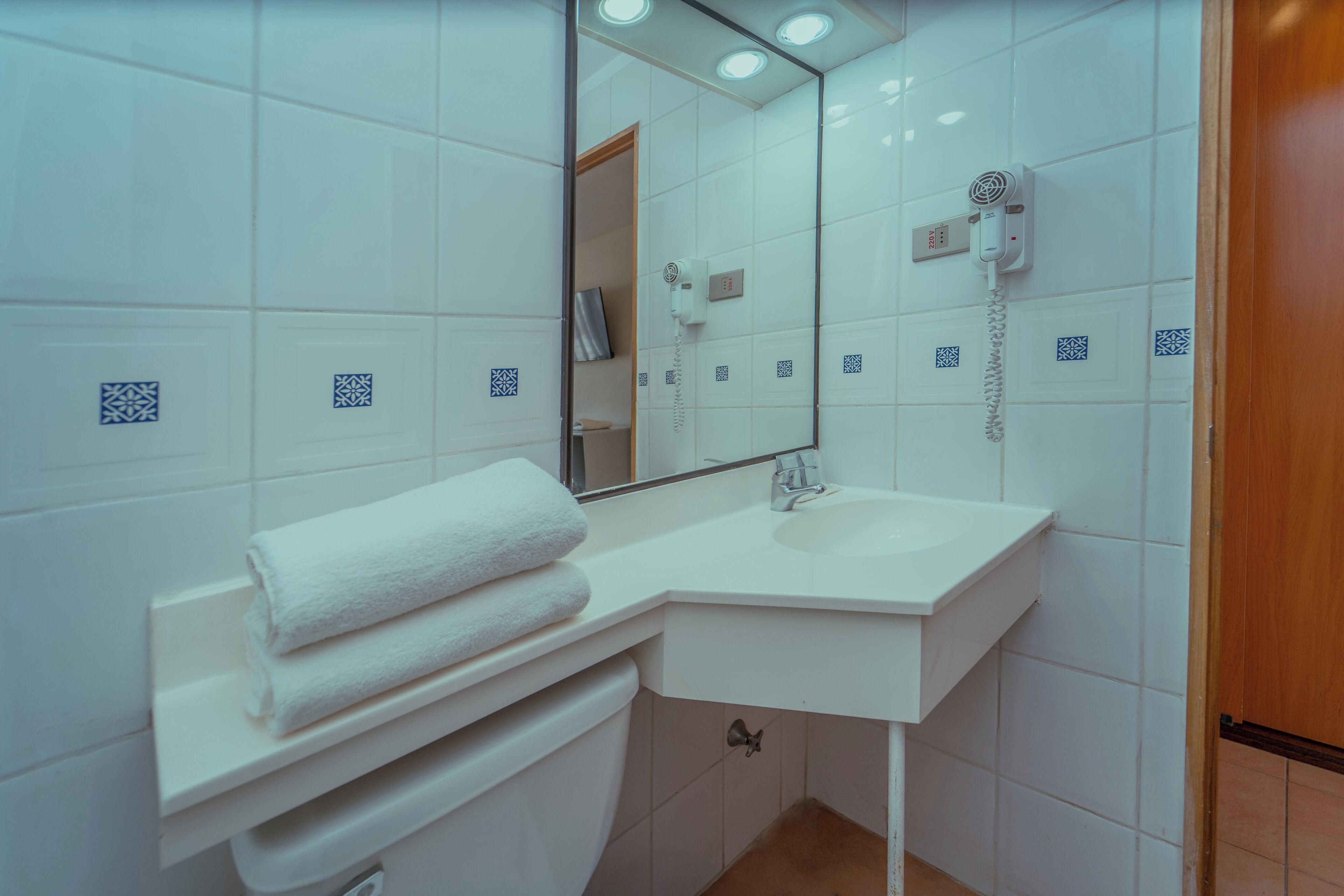 Un baño con un lavamanos blanco, un espejo y un secador de pelo montado en la pared.