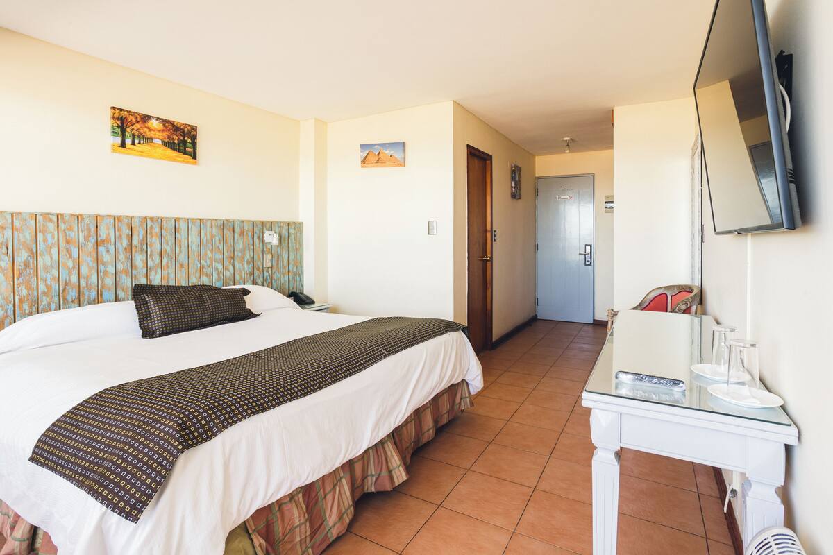 Ein Hotelzimmer mit Bett, Fernseher, Schreibtisch und einer Tür zu einem weiteren Raum.