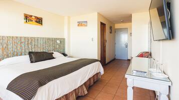 Quarto de hotel com cama, televisão, escrivaninha e porta que dá para outro espaço.