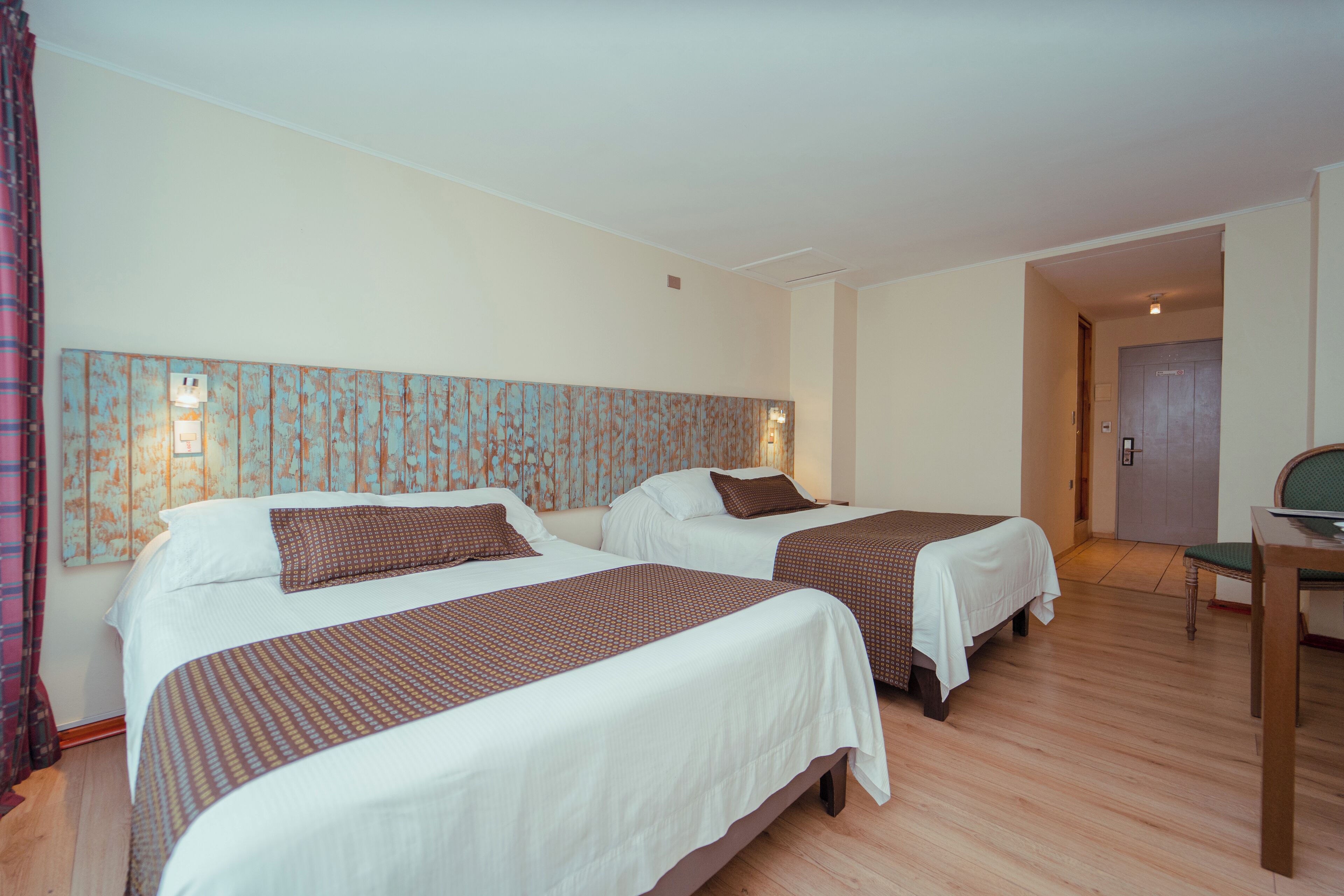 Een hotelkamer met twee bedden, een houten vloer, een bureau en een stoel.