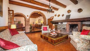 A spacious living room with a fireplace, wooden beams, and patterned sofas. - Villa Le Liscaie [Crete Senesi]. (Asciano)