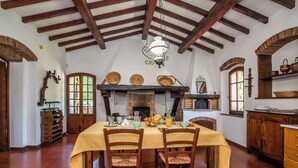 A dining area with a high ceiling, wooden beams, a fireplace, and a table set for a meal. - Villa Le Liscaie [Crete Senesi]. (Asciano)