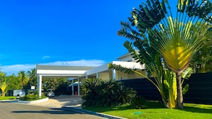 A modern building with a covered entrance, surrounded by lush greenery and a clear blue sky. - Harmonious 2-bedroom Apartment with AC, WiFi & Balcony in marvelous Puerto Plata (Puerto Plata)