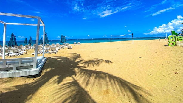 A beach with a clear sky, a volleyball net, and sun umbrellas. - Harmonious 2-bedroom Apartment with AC, WiFi & Balcony in marvelous Puerto Plata (Puerto Plata)