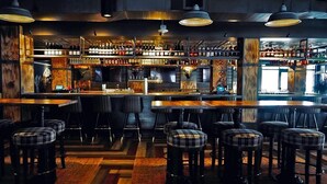 Zona de bar con varios taburetes y una barra provista de botellas.