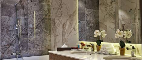 Un baño moderno con pared de mármol, un espejo grande, una bañera y un tocador con lavabo y toallero.
