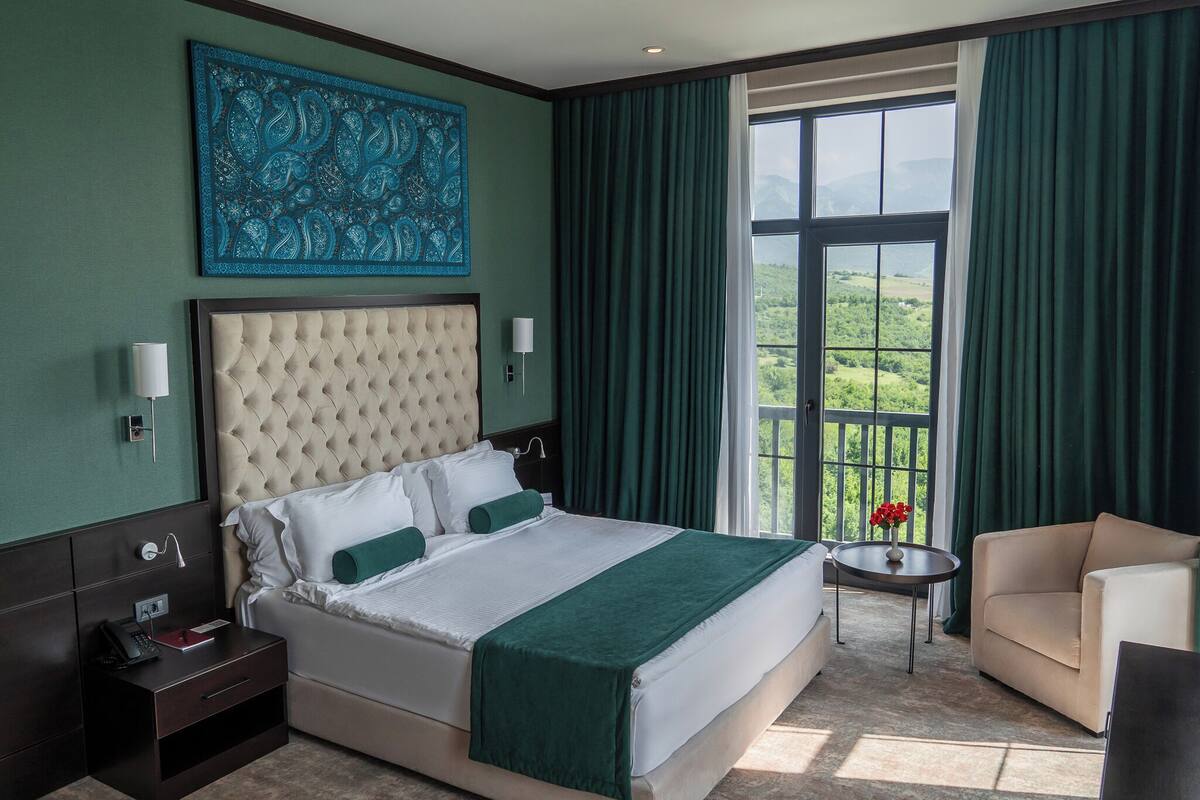 A hotel room with a large bed, a view of the outdoors, a small table with a vase of flowers, and a sofa.