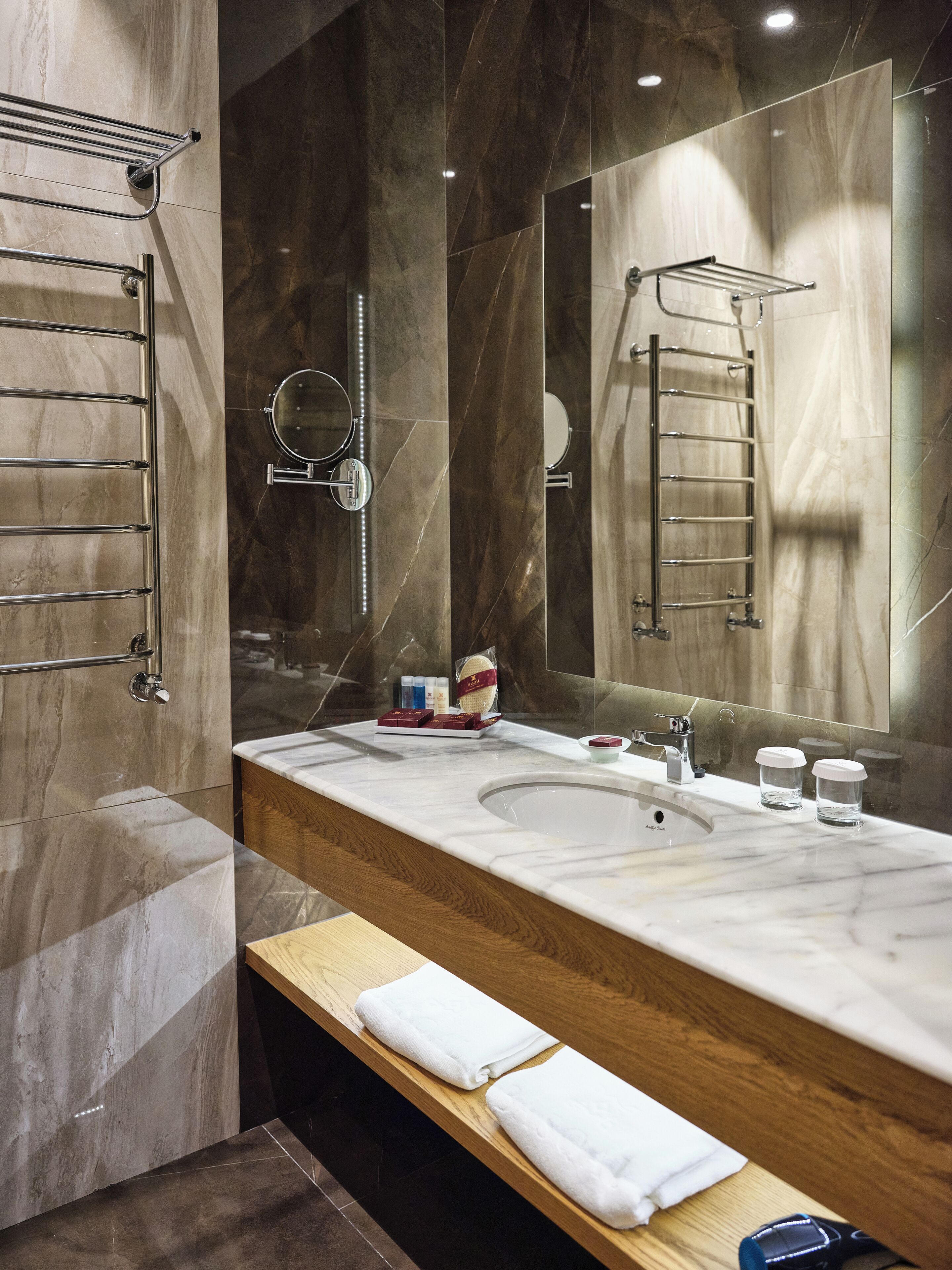 Un baño moderno con tocador de mármol, un espejo grande y un perchero.