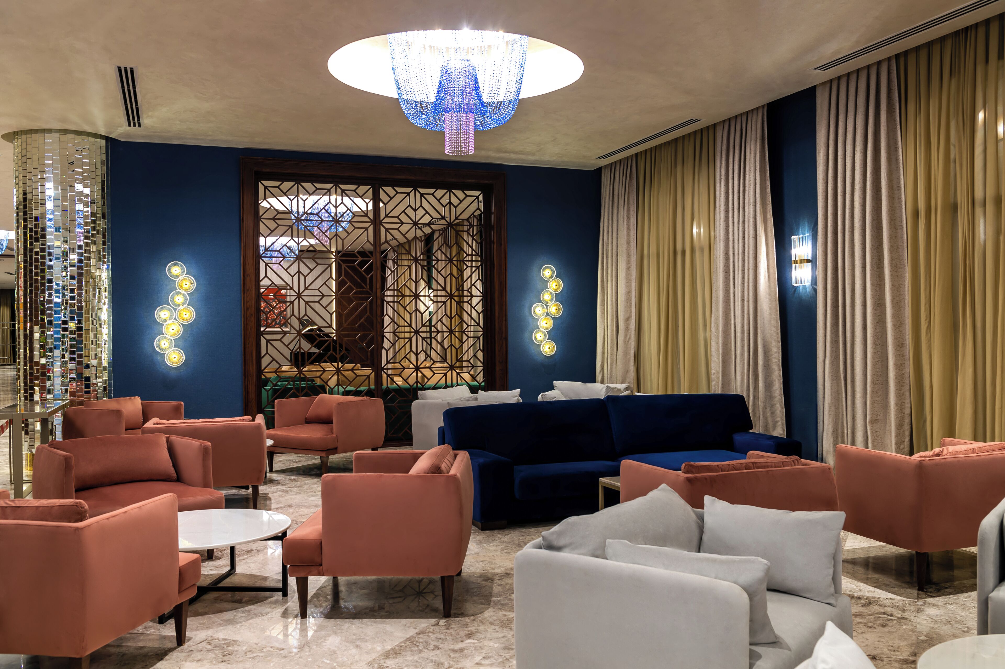 Een hal met een blauwe muur, een kroonluchter en een zithoek met banken en fauteuils.
