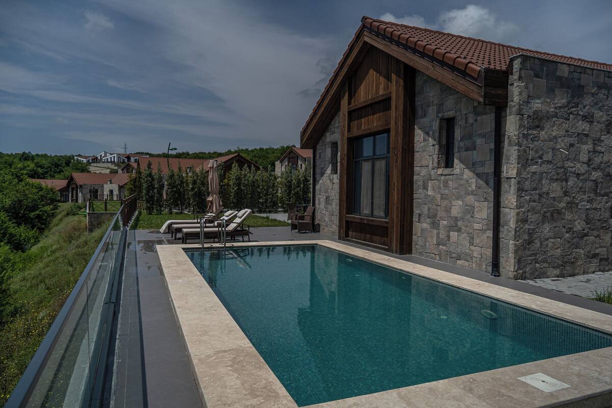 A modern pool area with a stone building, lounge chairs, and a clear view of the surrounding landscape.