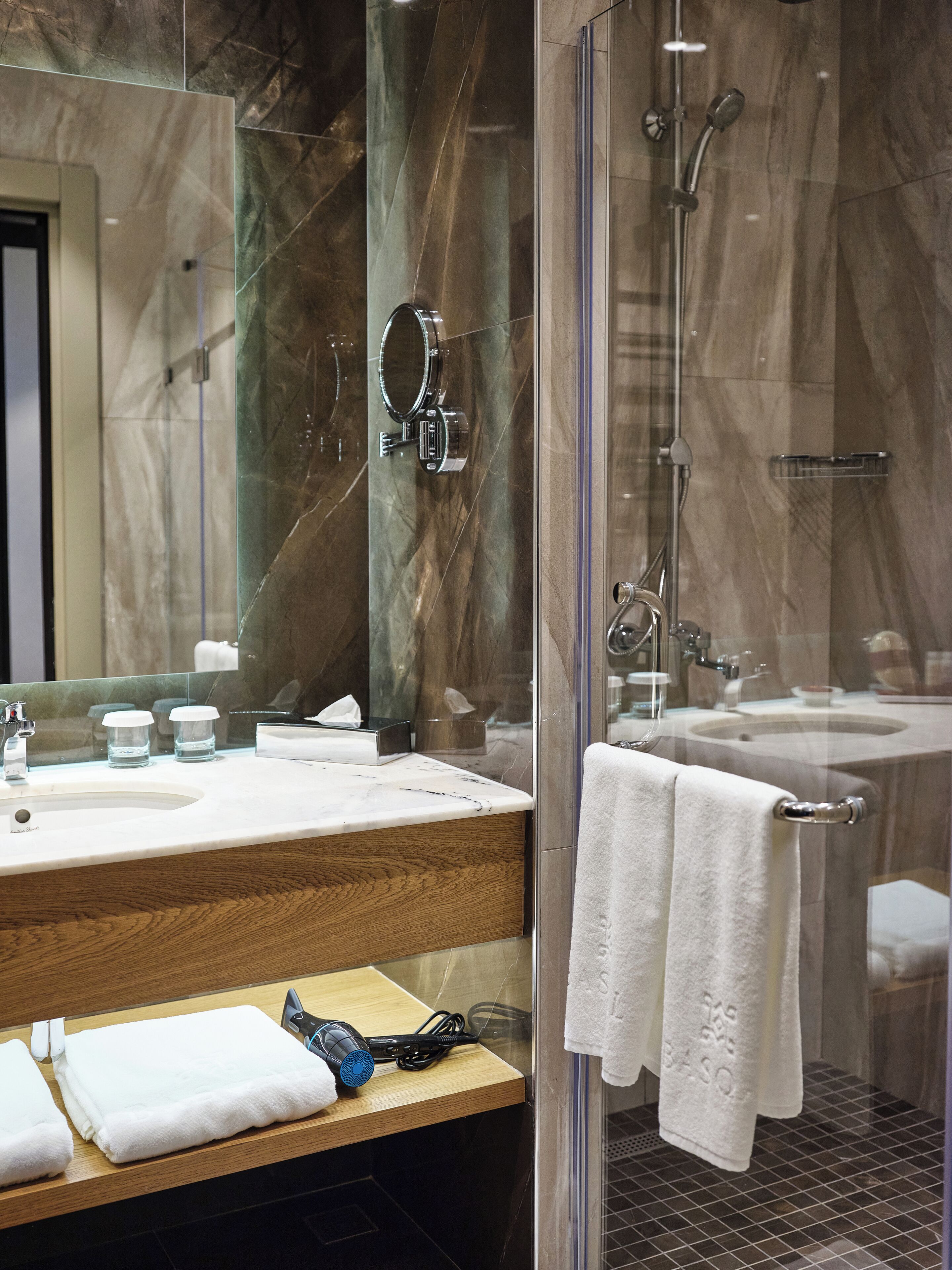 A modern bathroom with a glass-enclosed shower, a marble vanity, and a large mirror.