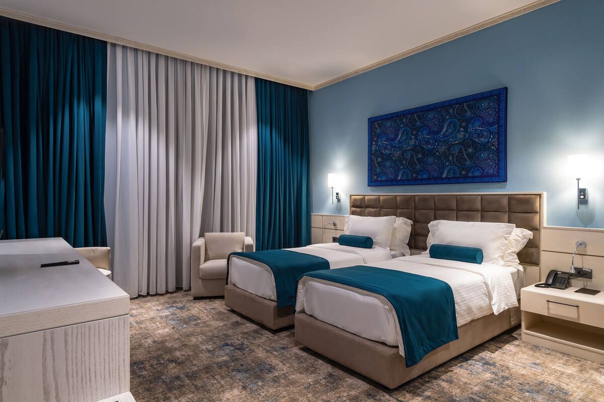 A hotel room with two beds, a desk, a chair, and a large abstract painting on the wall.