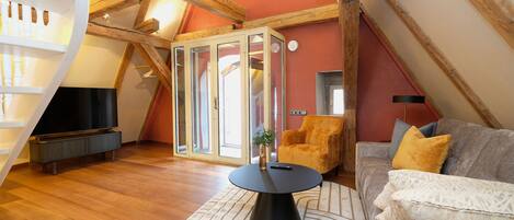 Ein gemütliches Loft-Wohnzimmer mit einem modernen schwarzen Couchtisch, einer bequemen Couch mit Kissen, einem Holzstuhl und einem Fernseher.