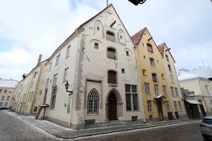 A historic building with a prominent arched entrance, multiple windows, and a tiled roof.