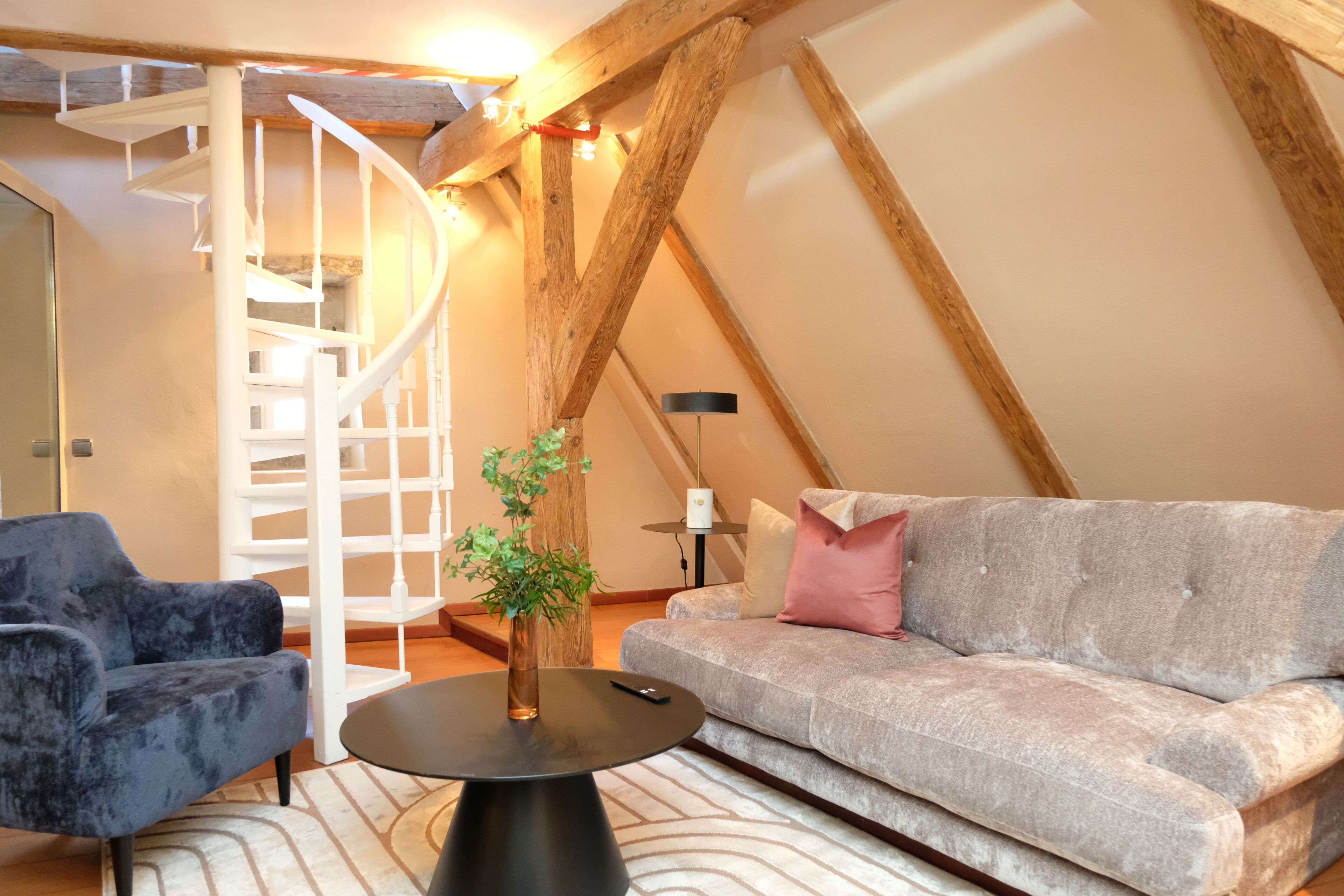 A loft-style room with a staircase, a sofa, a chair, and a small table.