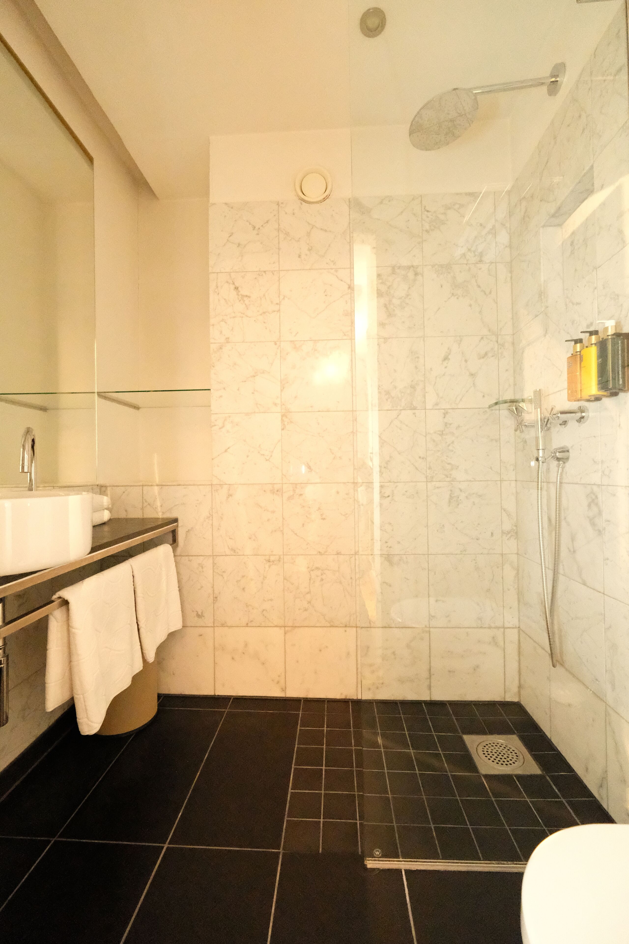 A modern bathroom with a marble shower, a sink, and a toilet.
