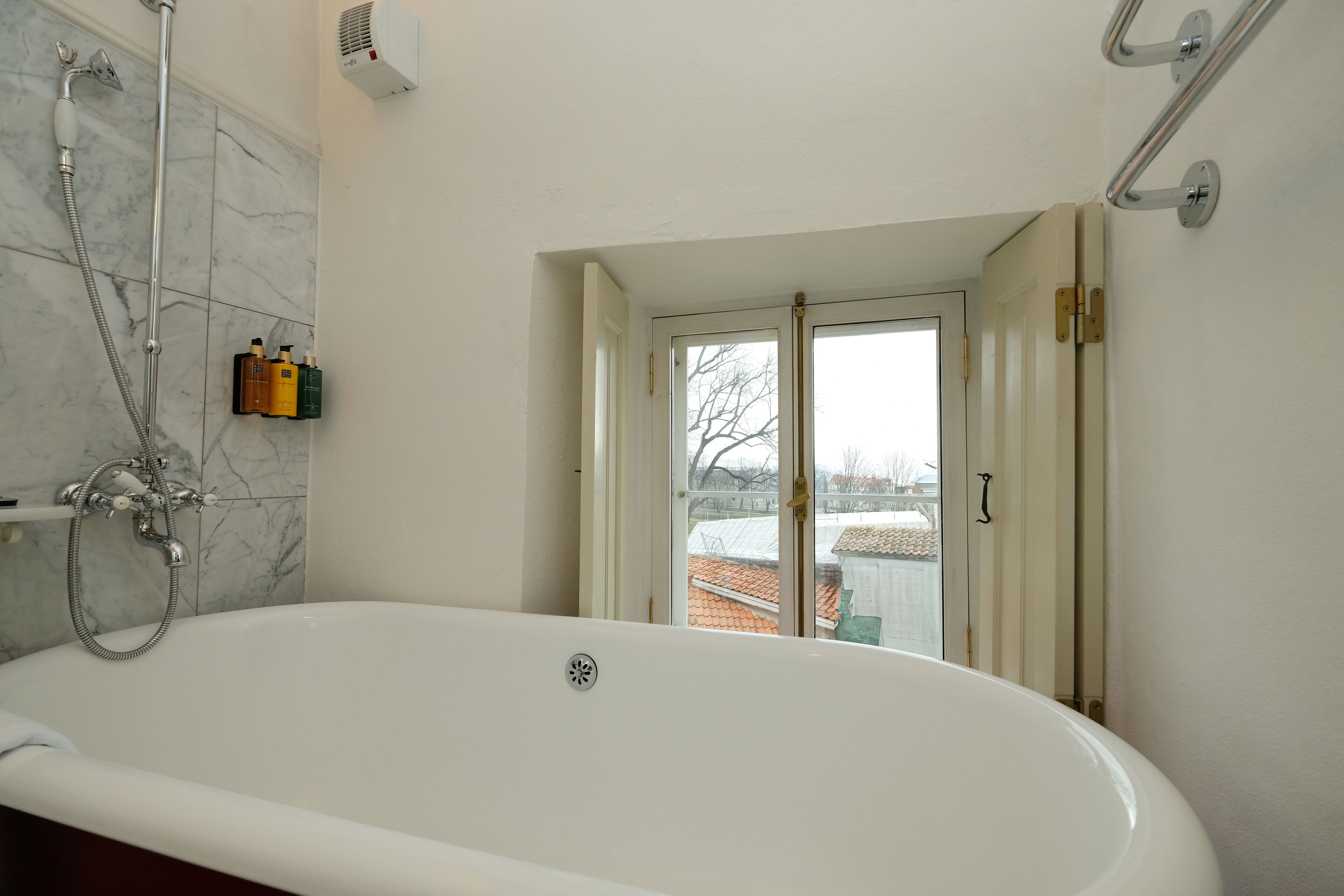Un bagno con una vasca da bagno bianca, una doccetta e una finestra vista casa.