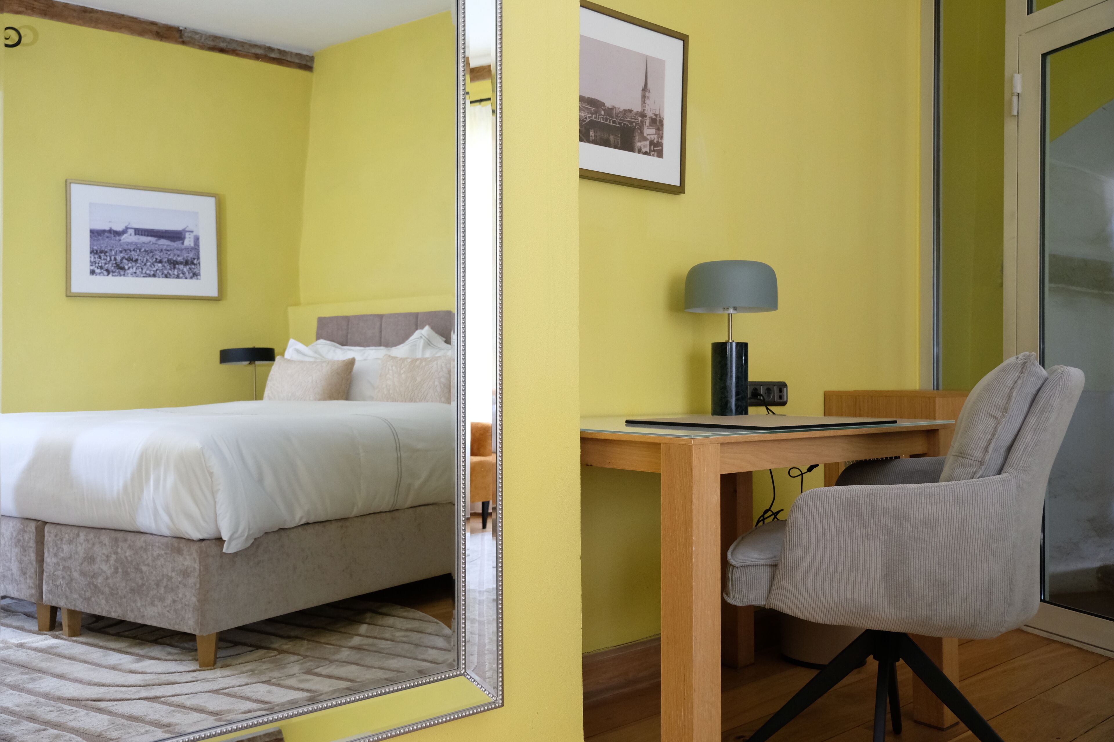 A hotel room with a bed, a desk, a chair, and a mirror.