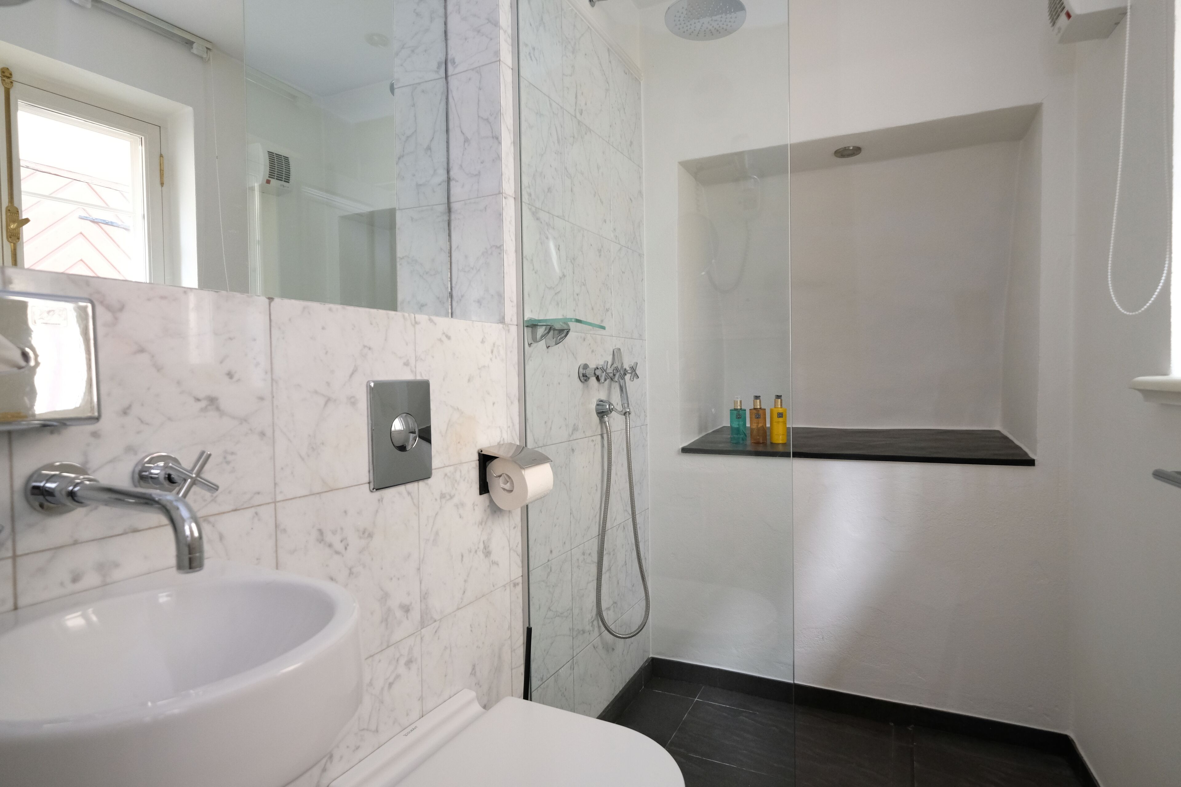 Un baño moderno con lavamanos de mármol, cabina de ducha con mampara de vidrio y un inodoro blanco.