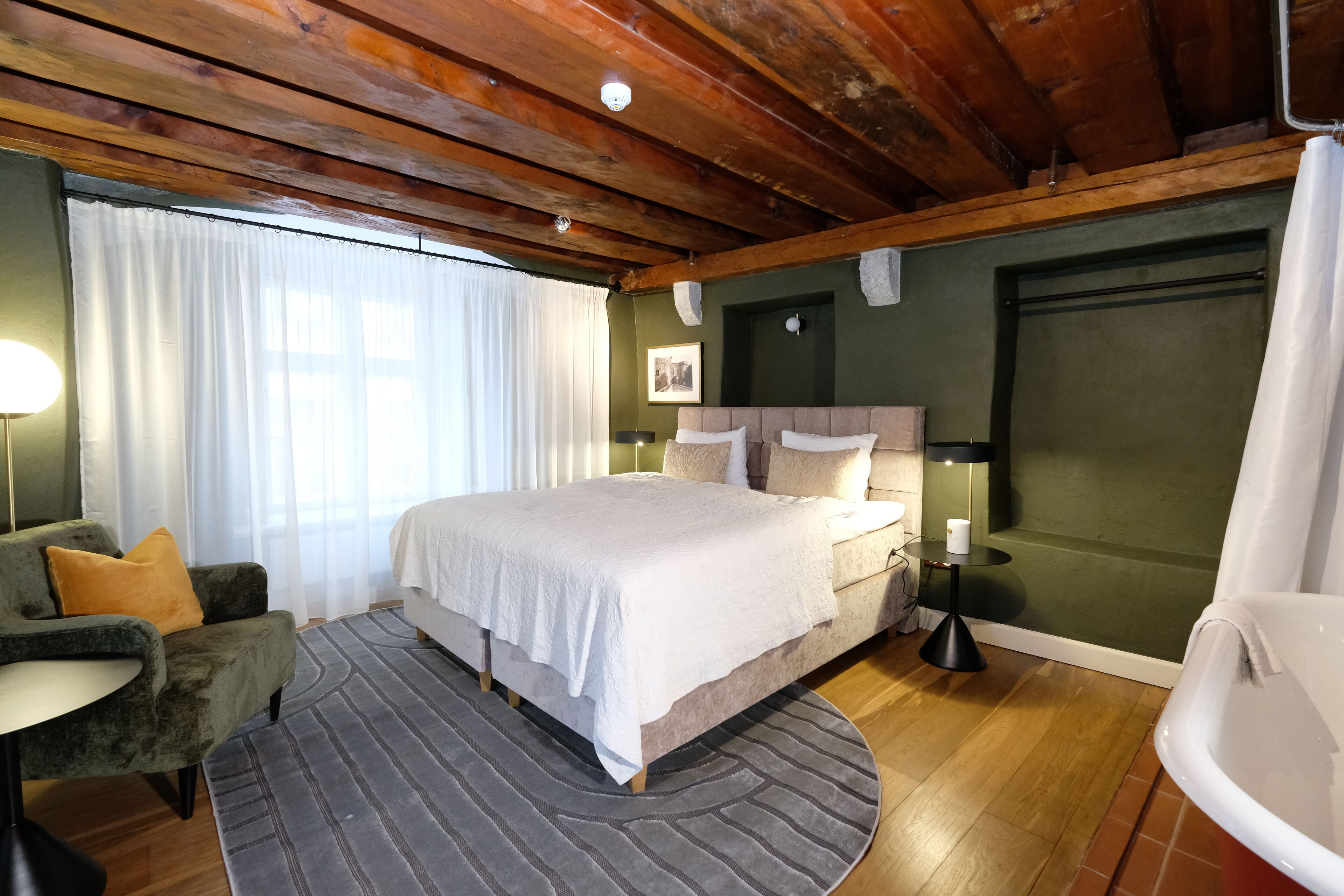 A bedroom with a bed, a chair, a bedside table, a lamp, and a bathtub.