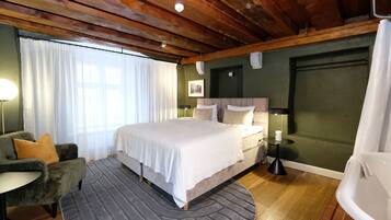 A bedroom with a bed, a chair, a bedside table, a lamp, and a bathtub.