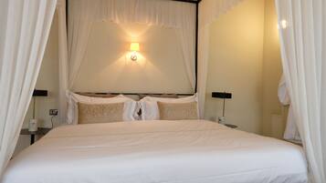 A neatly made bed with white bedding and a canopy, a bedside lamp, and a wall-mounted light fixture.