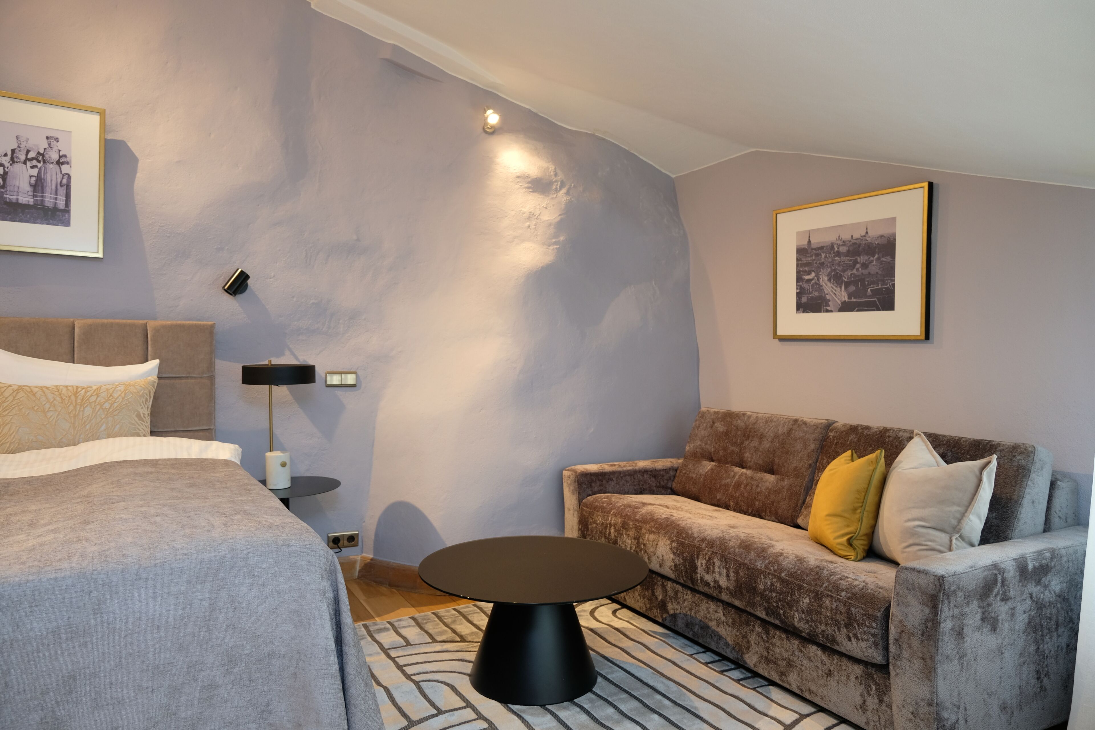 Une chambre à coucher moderne avec un lit, un canapé, une table basse ronde et deux tableaux encadrés accrochés au mur.