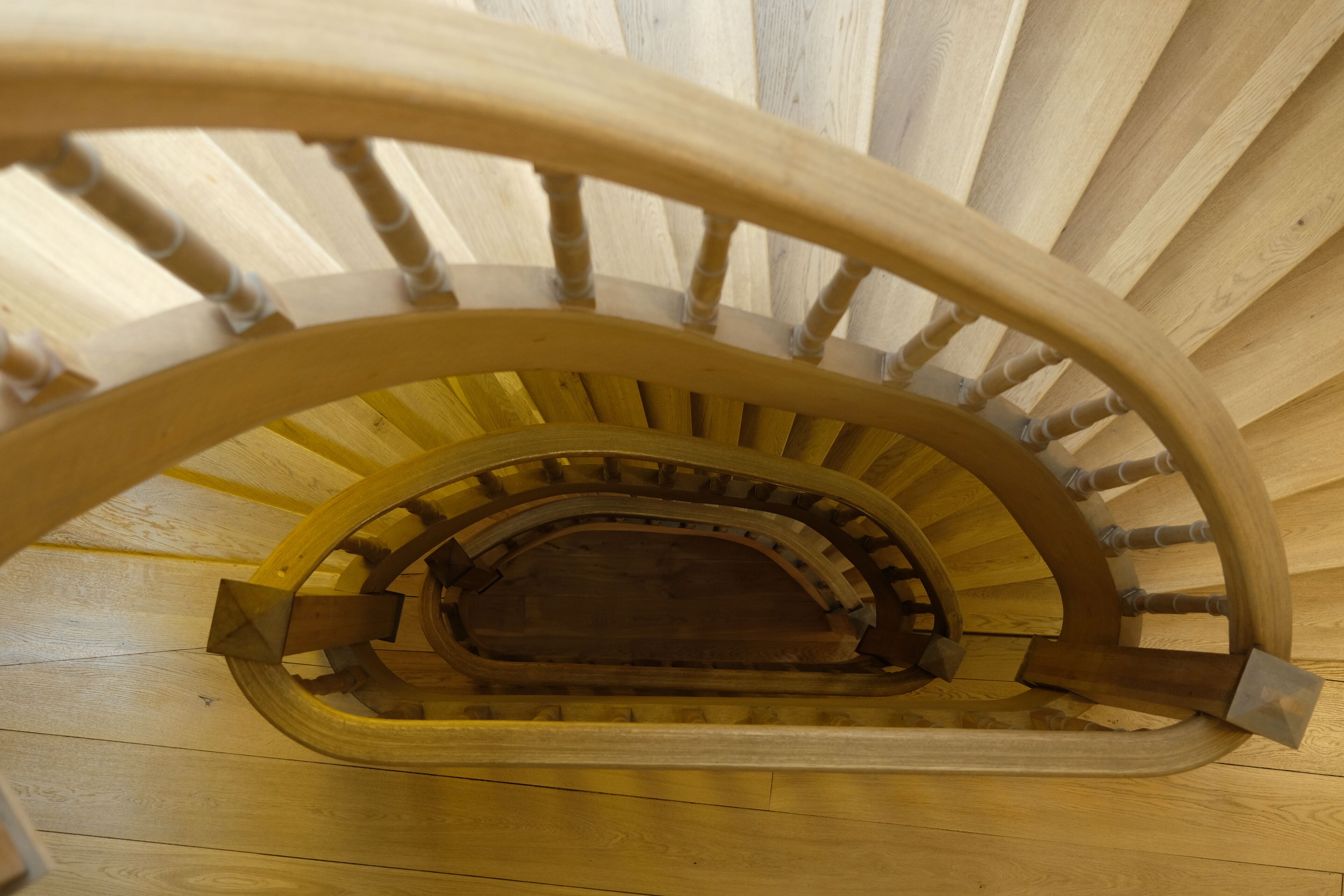 A wooden spiral staircase with a central handrail and steps made of wood.